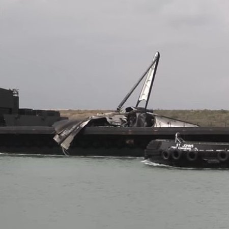 Damaged Falcon 9 booster laying on its side on drone ship as it returns to port